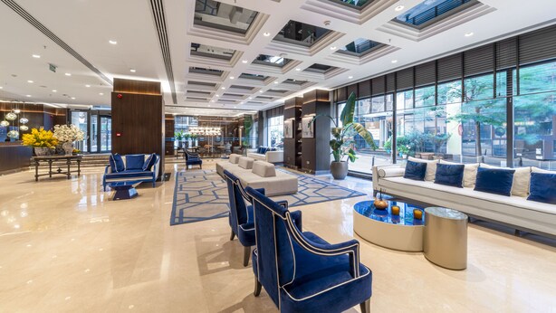Un hall d’entrée spacieux au design moderne, comprenant un espace détente avec des canapés et des fauteuils, un comptoir d’accueil et de grandes fenêtres offrant une vue sur l’extérieur.