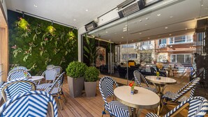 Un espace extérieur aménagé avec des tables et des chaises rondes, un mur végétal et une vue sur la ville grâce à de grandes fenêtres.