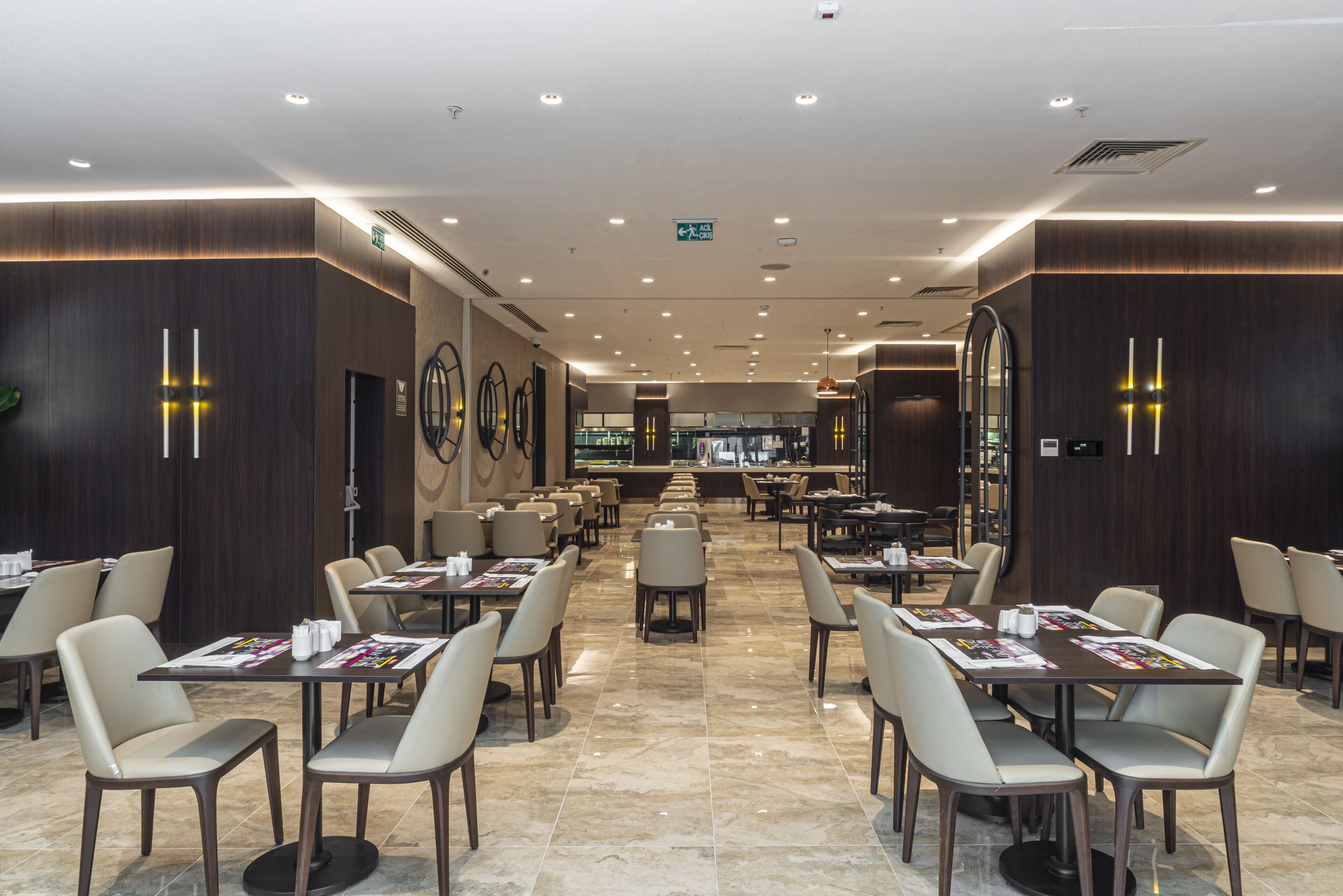 A spacious hotel lobby with multiple dining areas, modern decor, and a clear view of the restaurant in the background.