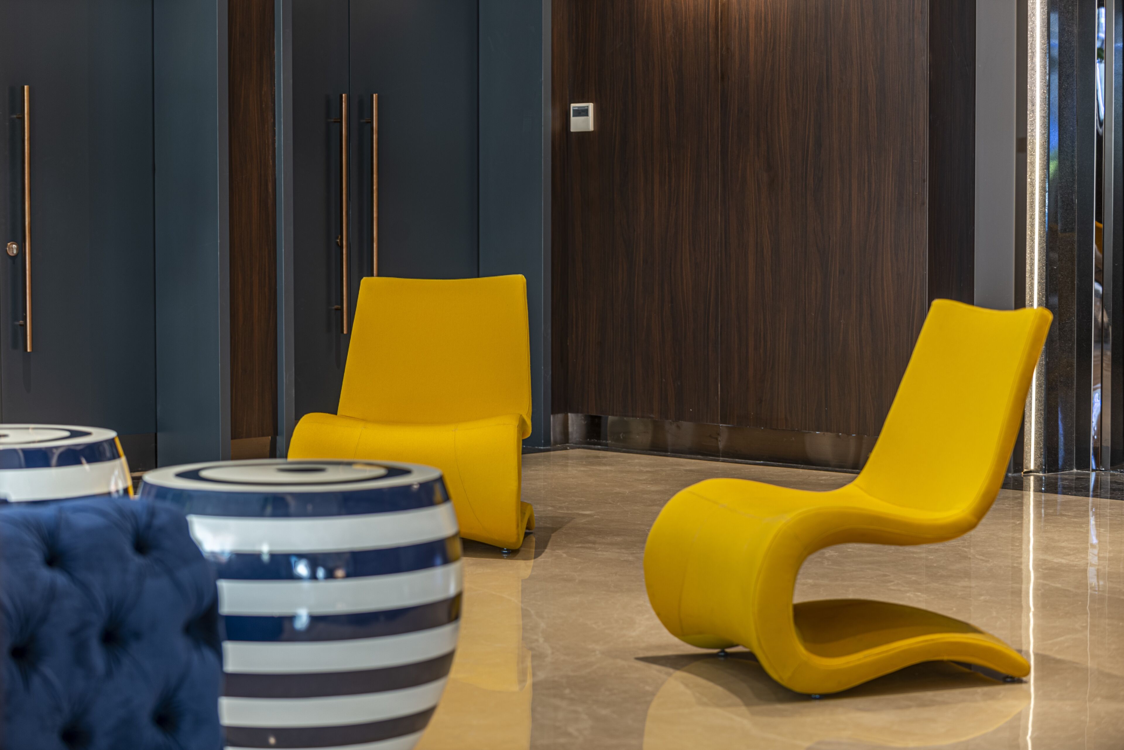 Eine moderne Lobby mit zwei gelben Sesseln, einem blau-weißen Streifenfußhocker und einem gepolsterten, blauen Sofa.