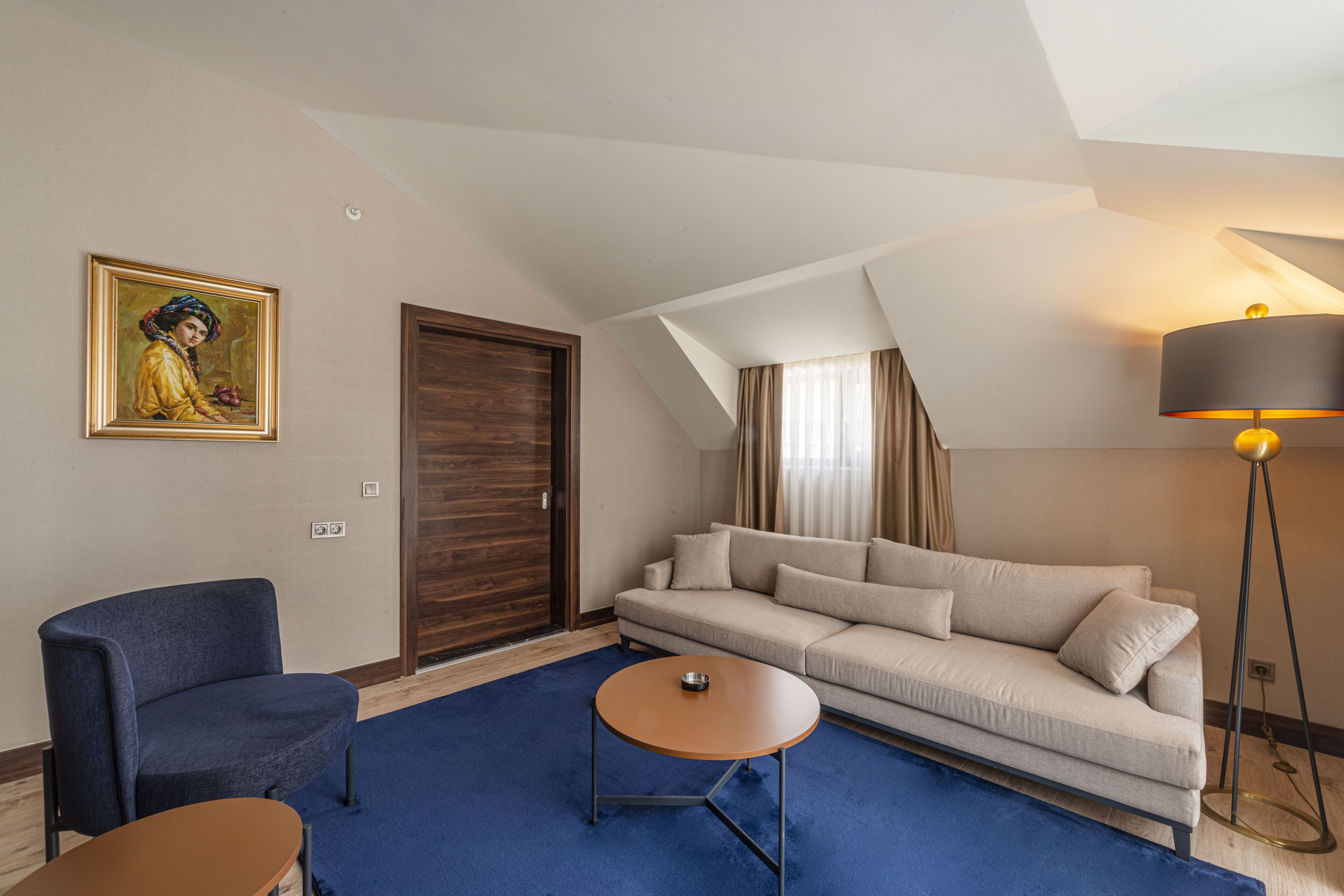 A modern living room with a blue carpet, a sofa, a chair, a coffee table, a painting, a door, and a floor lamp.