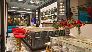 Un espace bar avec un comptoir, des tabourets de bar rouges et un grand vase rempli de fleurs rouges.