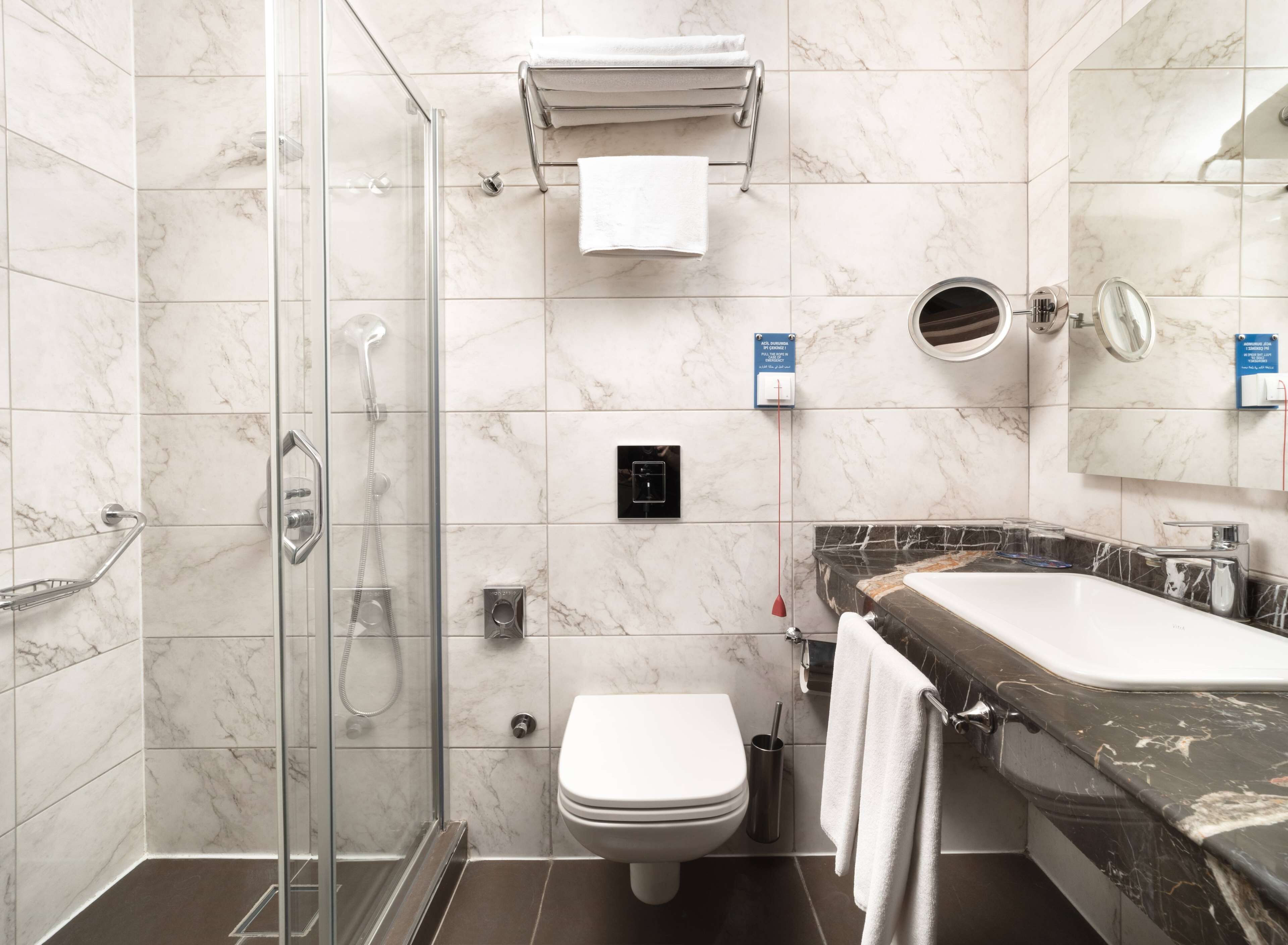 A modern bathroom with a glass-enclosed shower, a toilet, a sink with a marble countertop, and a towel rack.