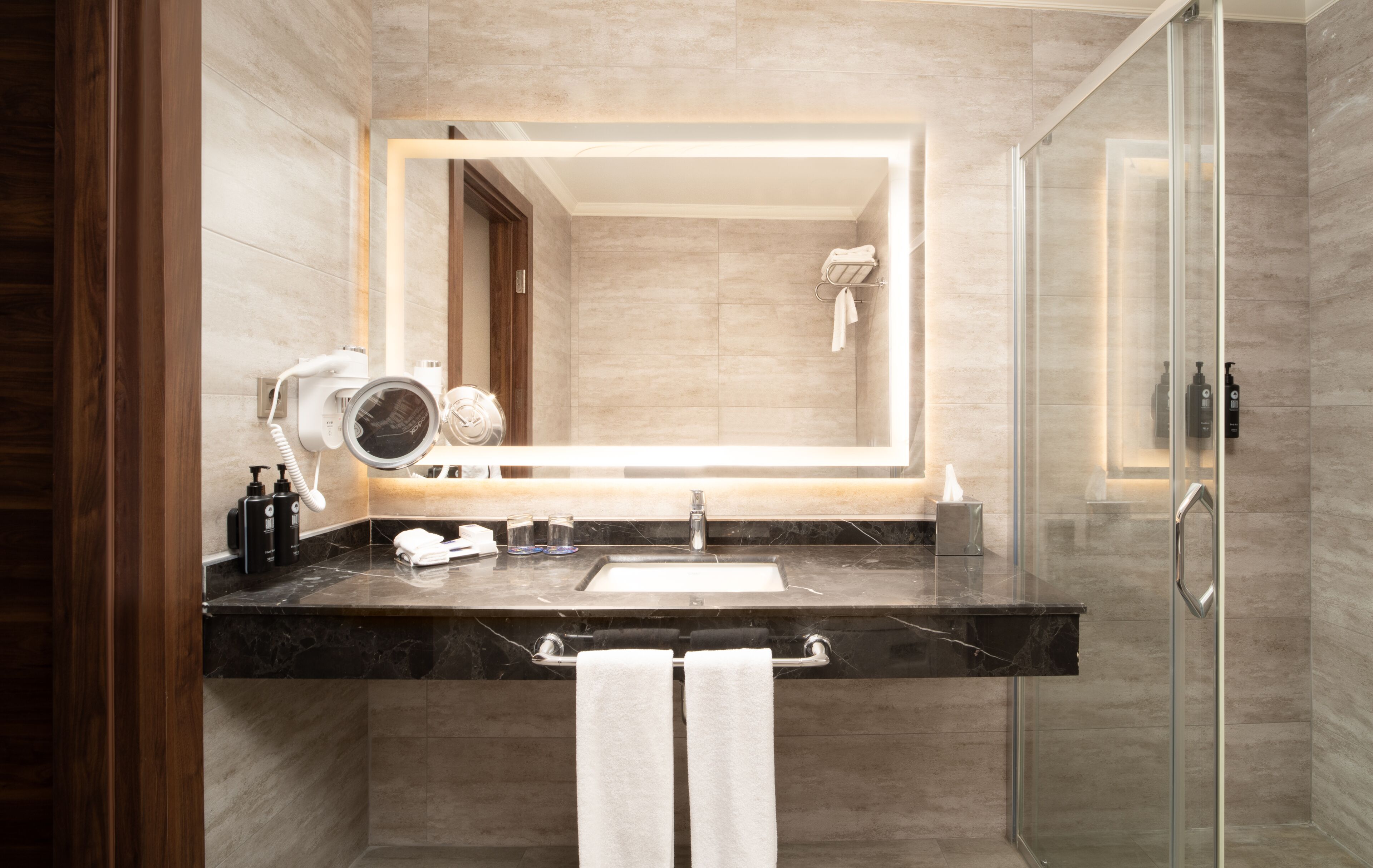 Een moderne badkamer met een grote spiegel, een haardroger, een wastafel en een douchecabine van glas.