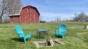 Un espacio al aire libre con césped, dos sillas Adirondack azules, una mesita y un brasero.