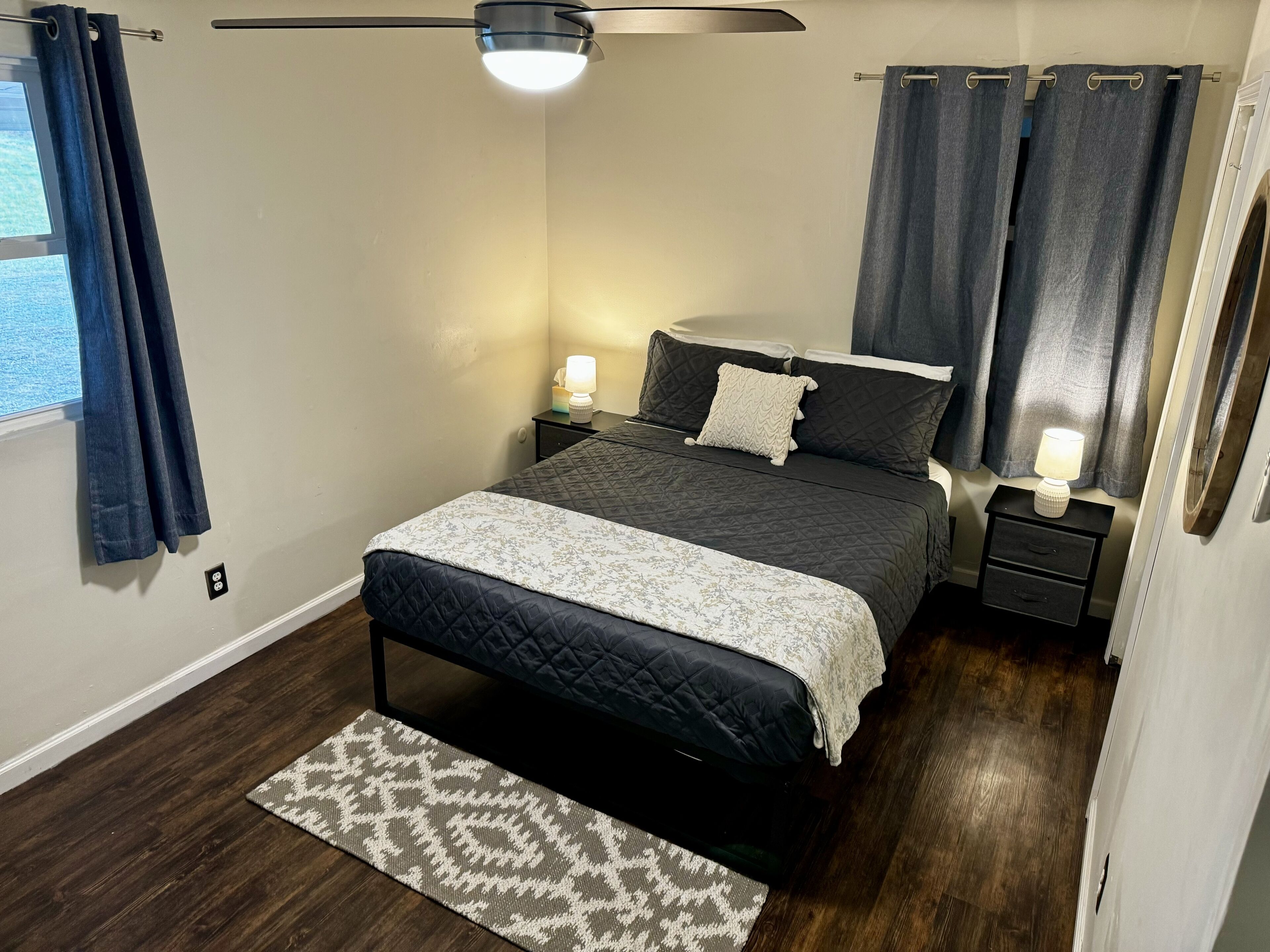 A bedroom with a bed, bedside lamps, a ceiling fan, and a window with curtains.