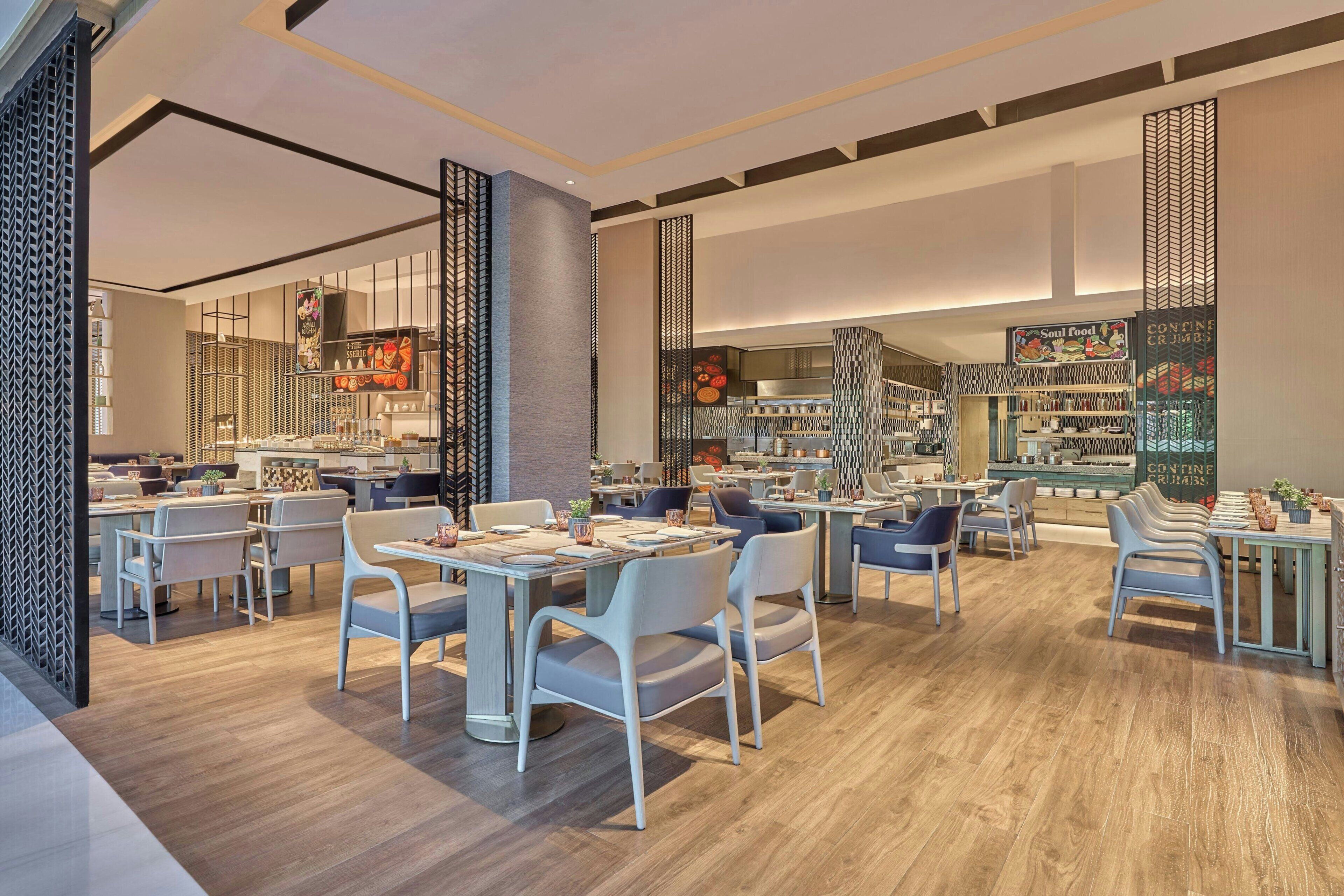 A modern restaurant with multiple dining areas, a kitchen in the background, and a variety of seating options.