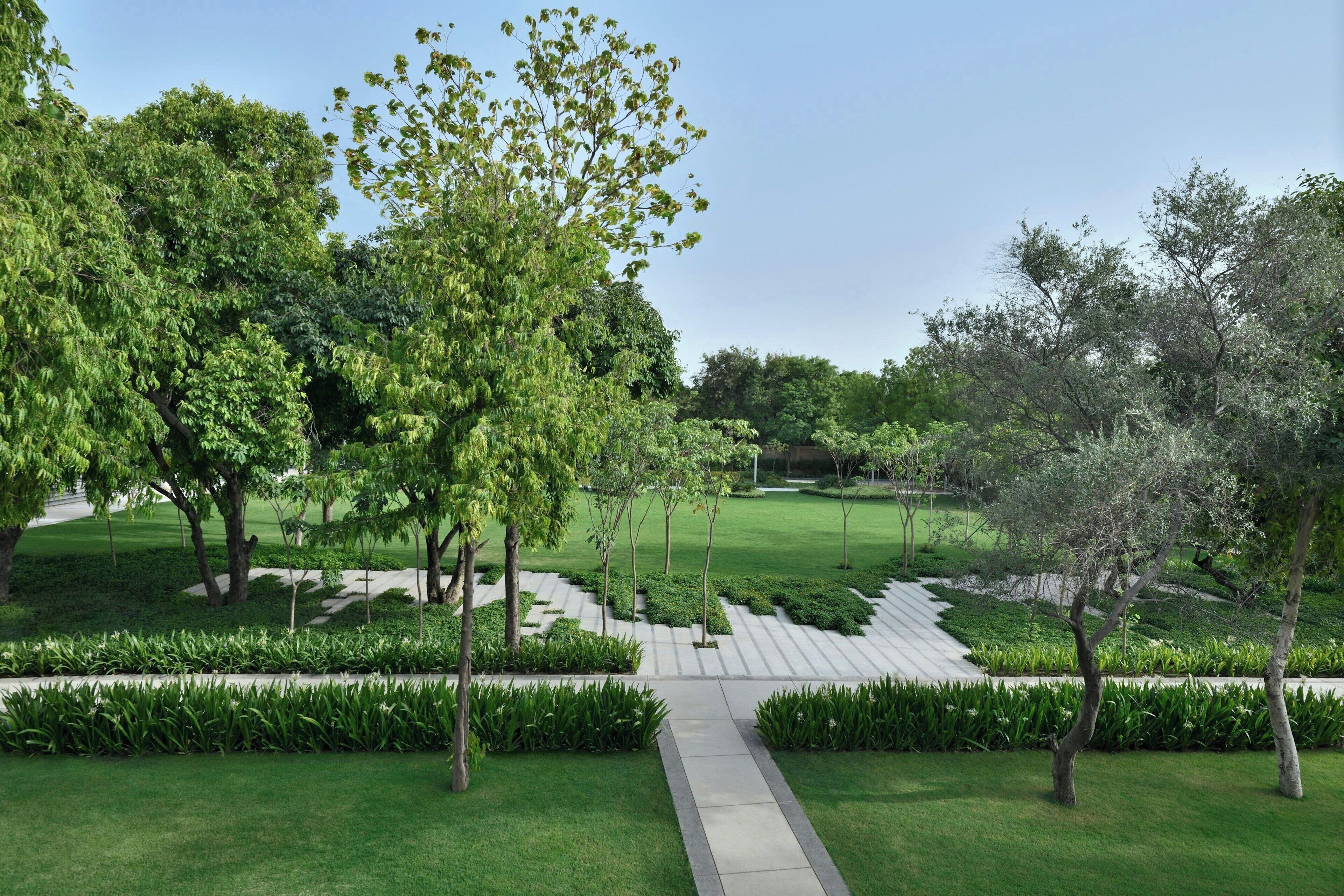 A landscaped garden with a central pathway, surrounded by neatly trimmed grass and trees.