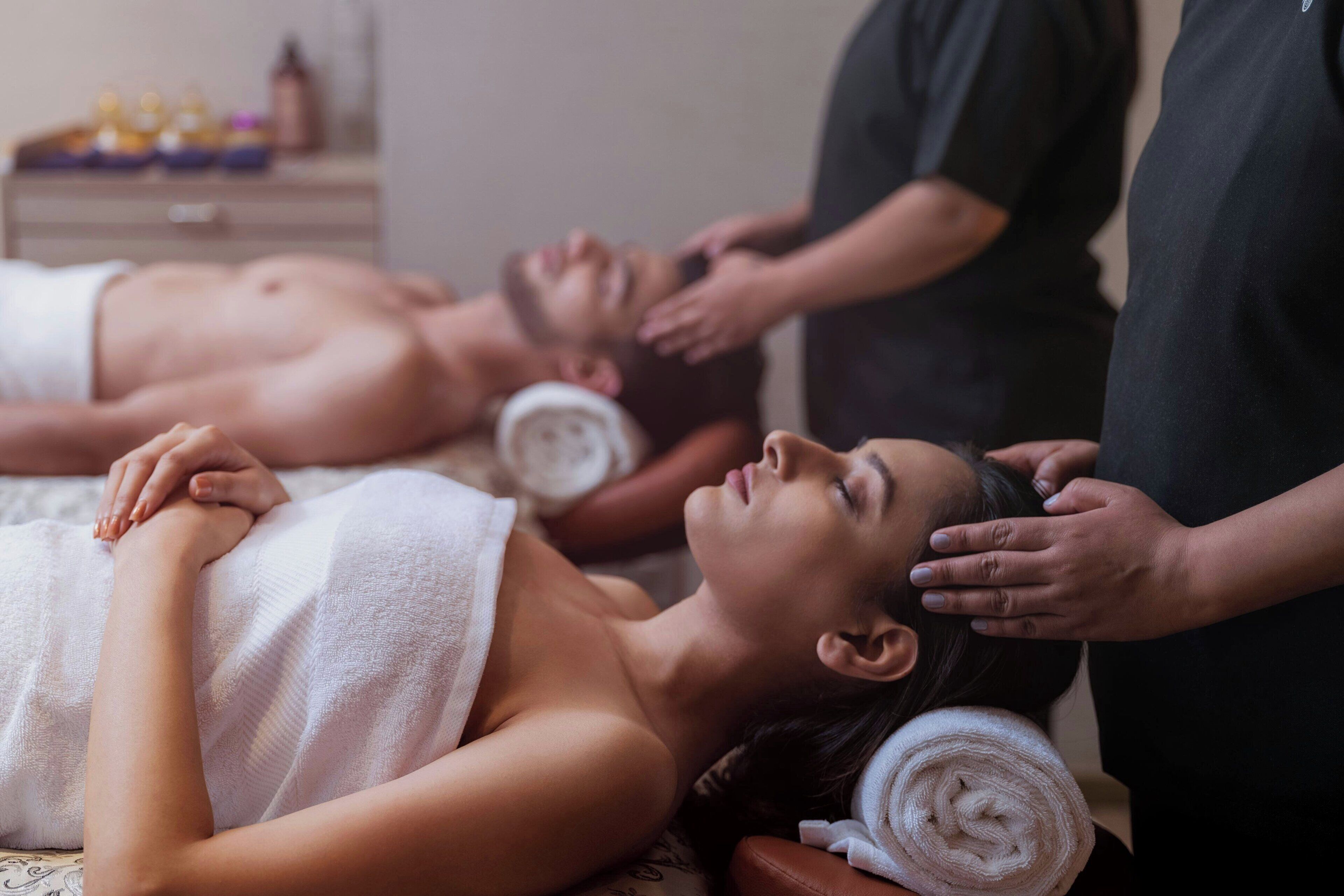 A massage therapy session with a client lying on a massage table, receiving head and neck massage from a therapist.
