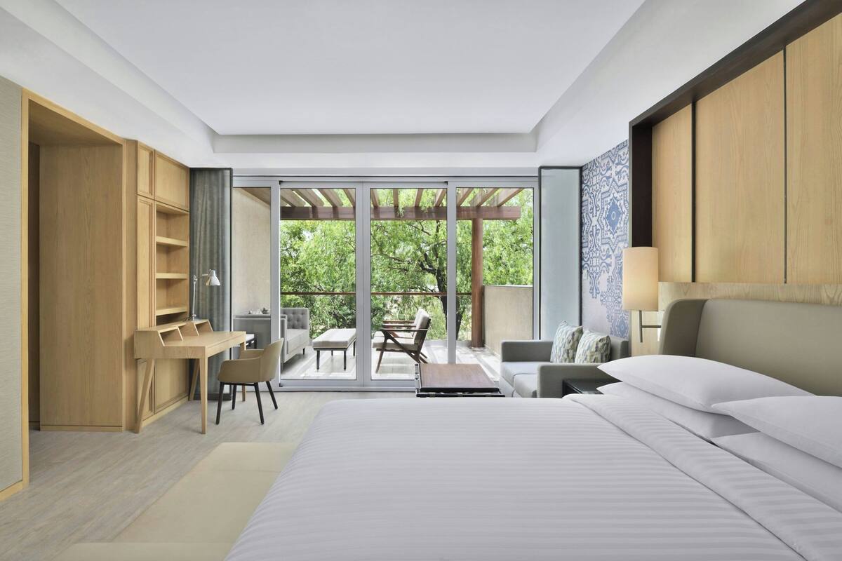 Un dormitorio moderno con una cama grande, un escritorio y un balcón con mobiliario exterior.