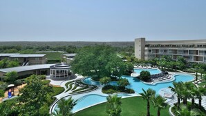 A resort with a large swimming pool, lush landscaping, and a multi-story building with balconies. - Aravali Marriott Resort & Spa, Delhi NCR (Faridabad)