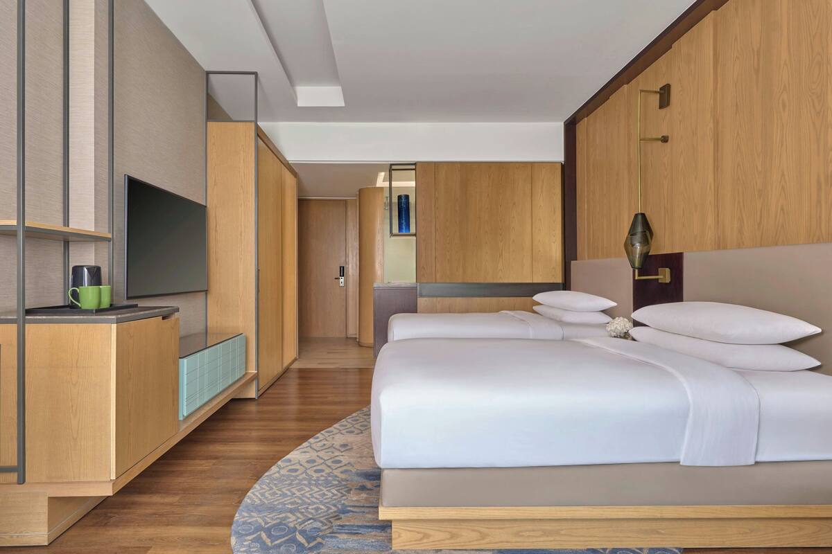 Una habitación de hotel con cama, televisión, escritorio con una taza y un armario de madera.