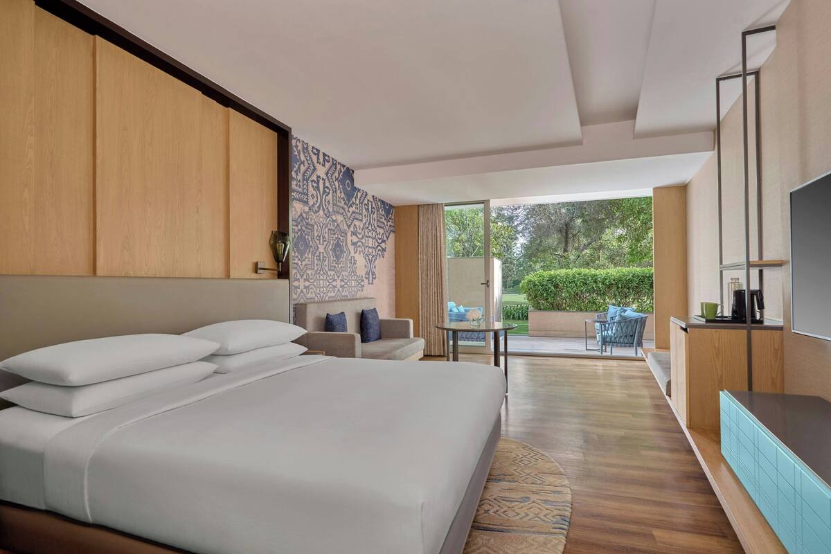 Habitación de hotel con una cama grande, un sofá, una mesita, un televisor y vistas al exterior.
