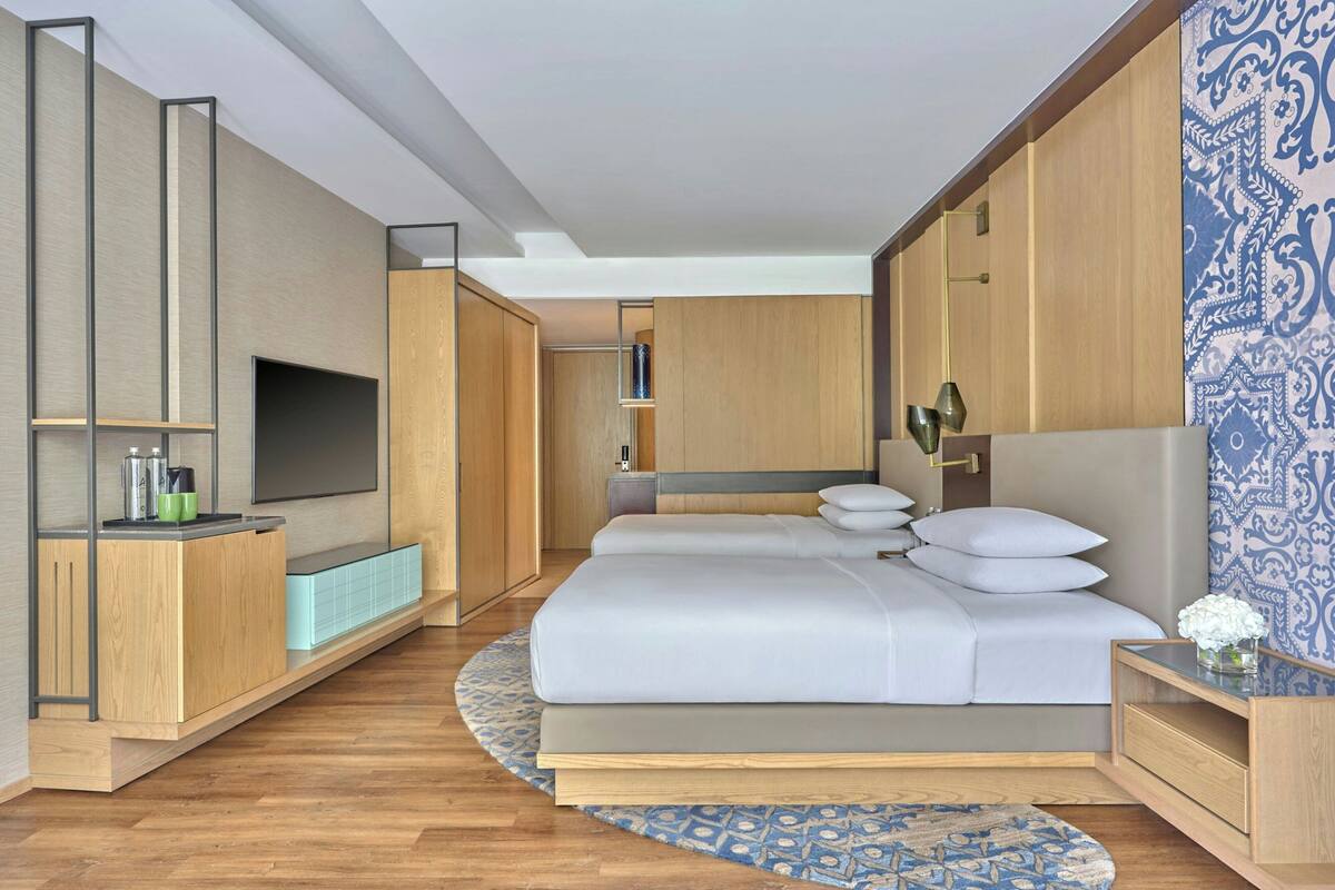 Una habitación de hotel moderna con una cama grande, televisión, muebles de madera y un papel tapiz estampado.