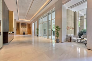 A spacious lobby with a polished floor, large windows, and a seating area with a sofa and armchairs.