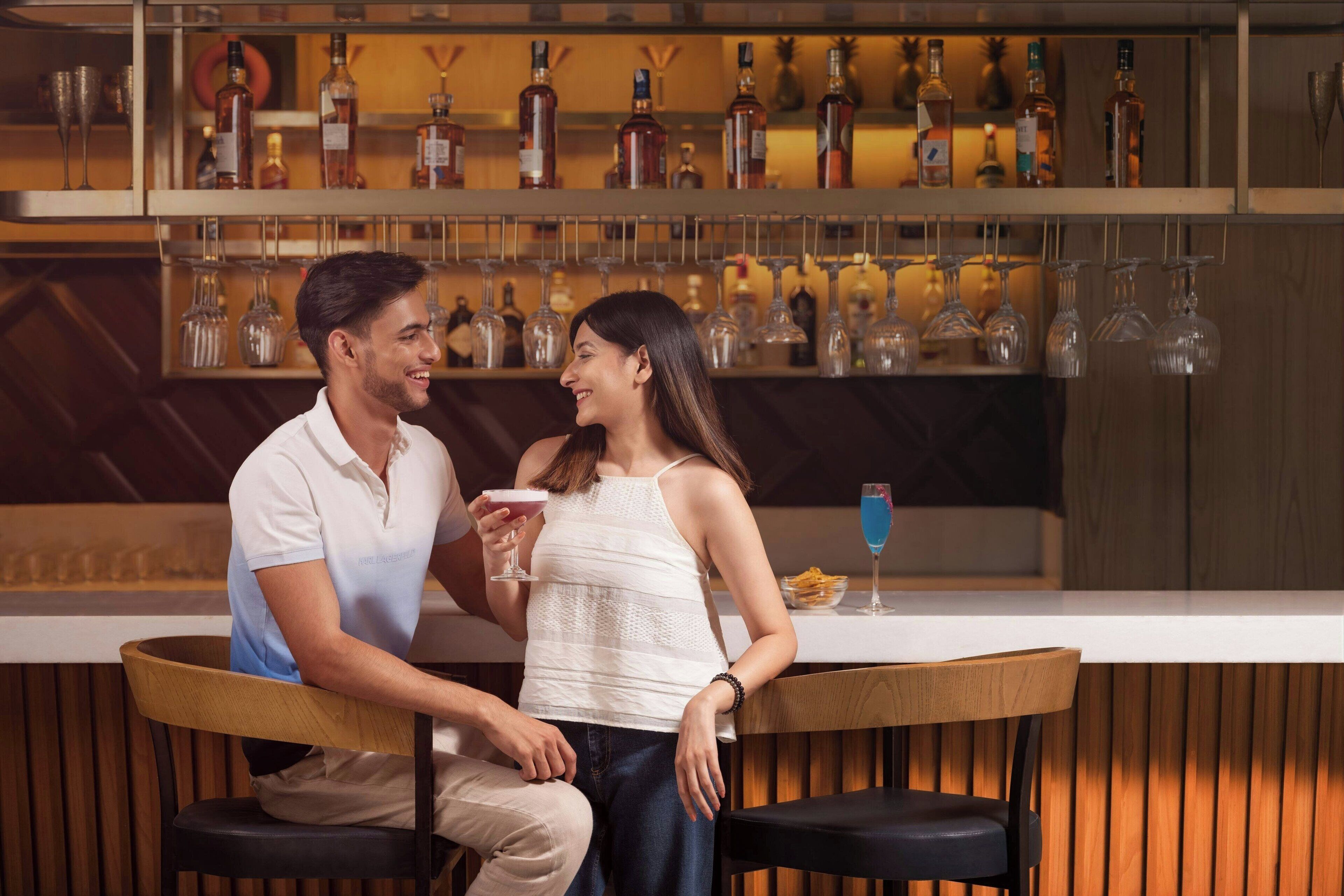A bar area with a counter, seating, and a variety of bottles and glasses on shelves.
