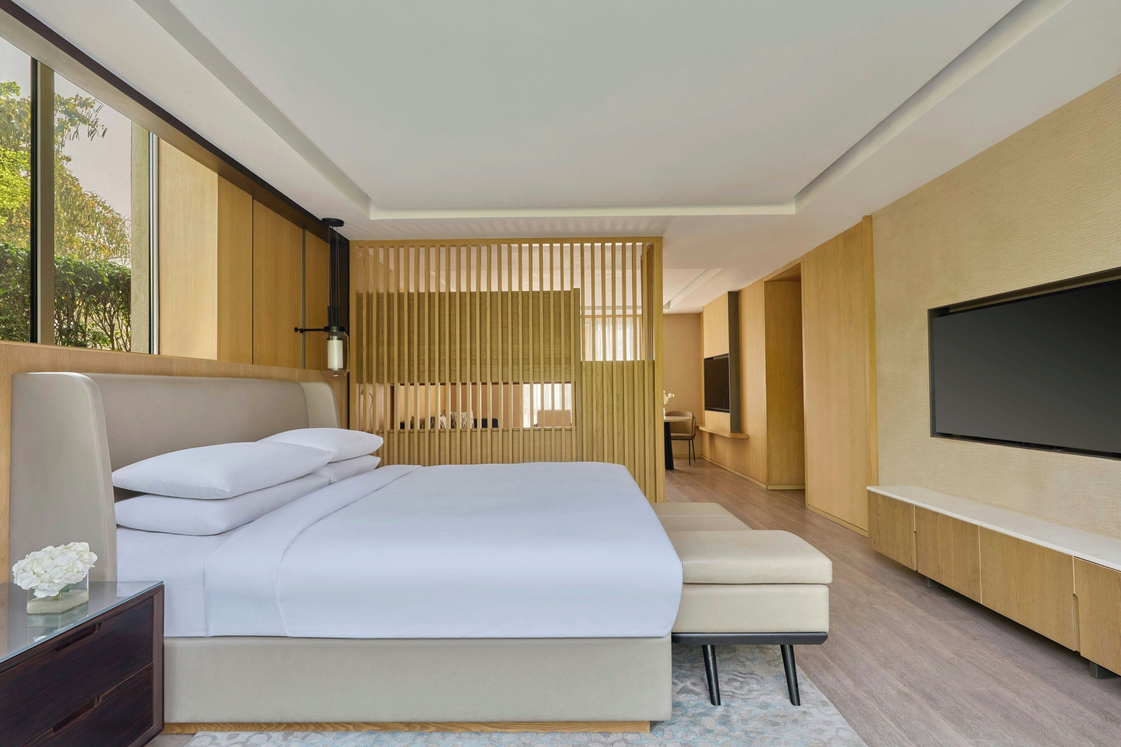 A modern bedroom with a large bed, a TV, and a seating area.