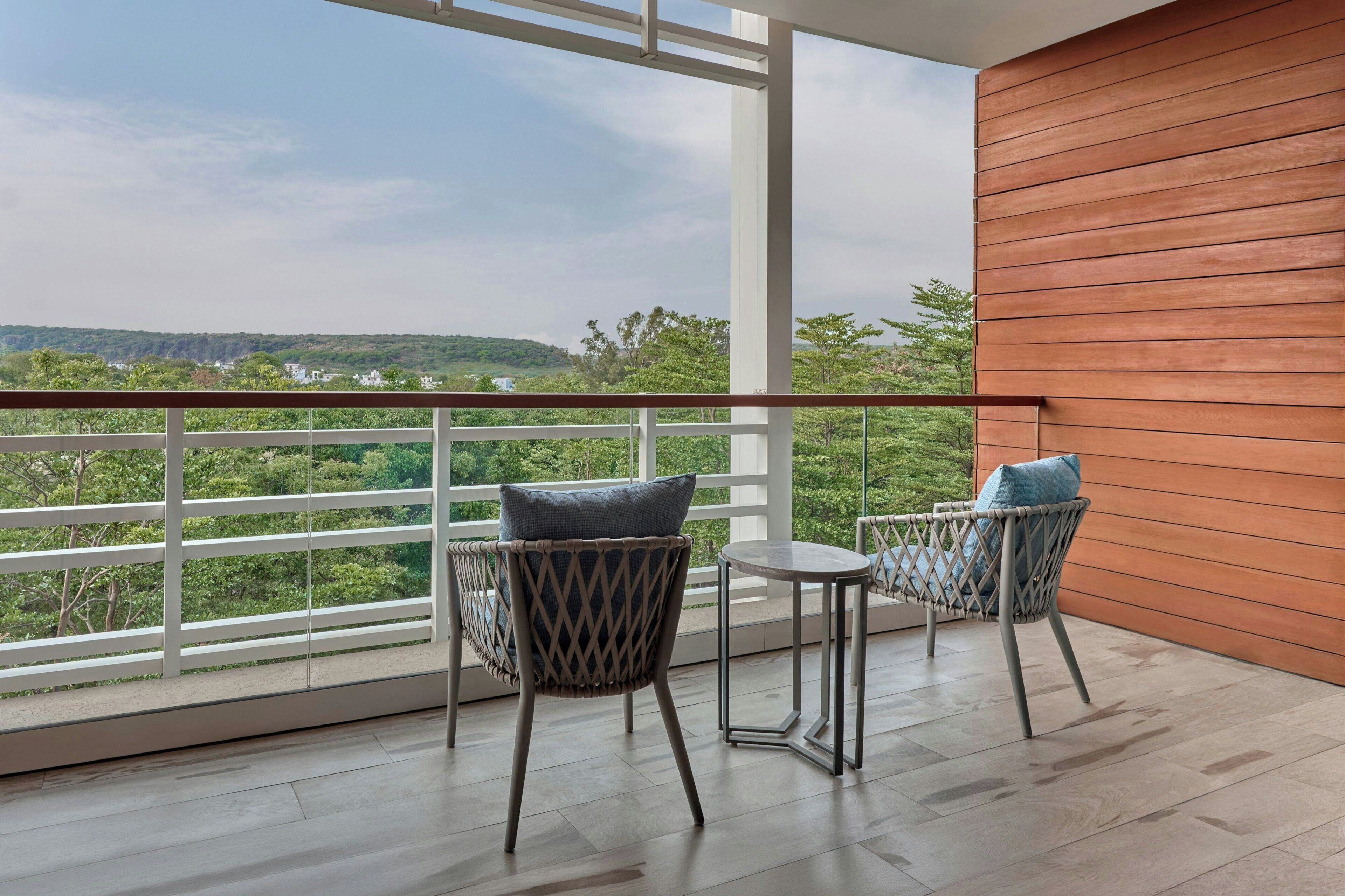Un balcon avec deux fauteuils en osier, une petite table et une vue sur la verdure et les collines.