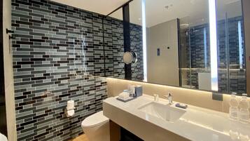 Un baño moderno con pared de mosaicos negros y grises, un inodoro blanco, un espejo grande y un lavamanos blanco con artículos de tocador.
