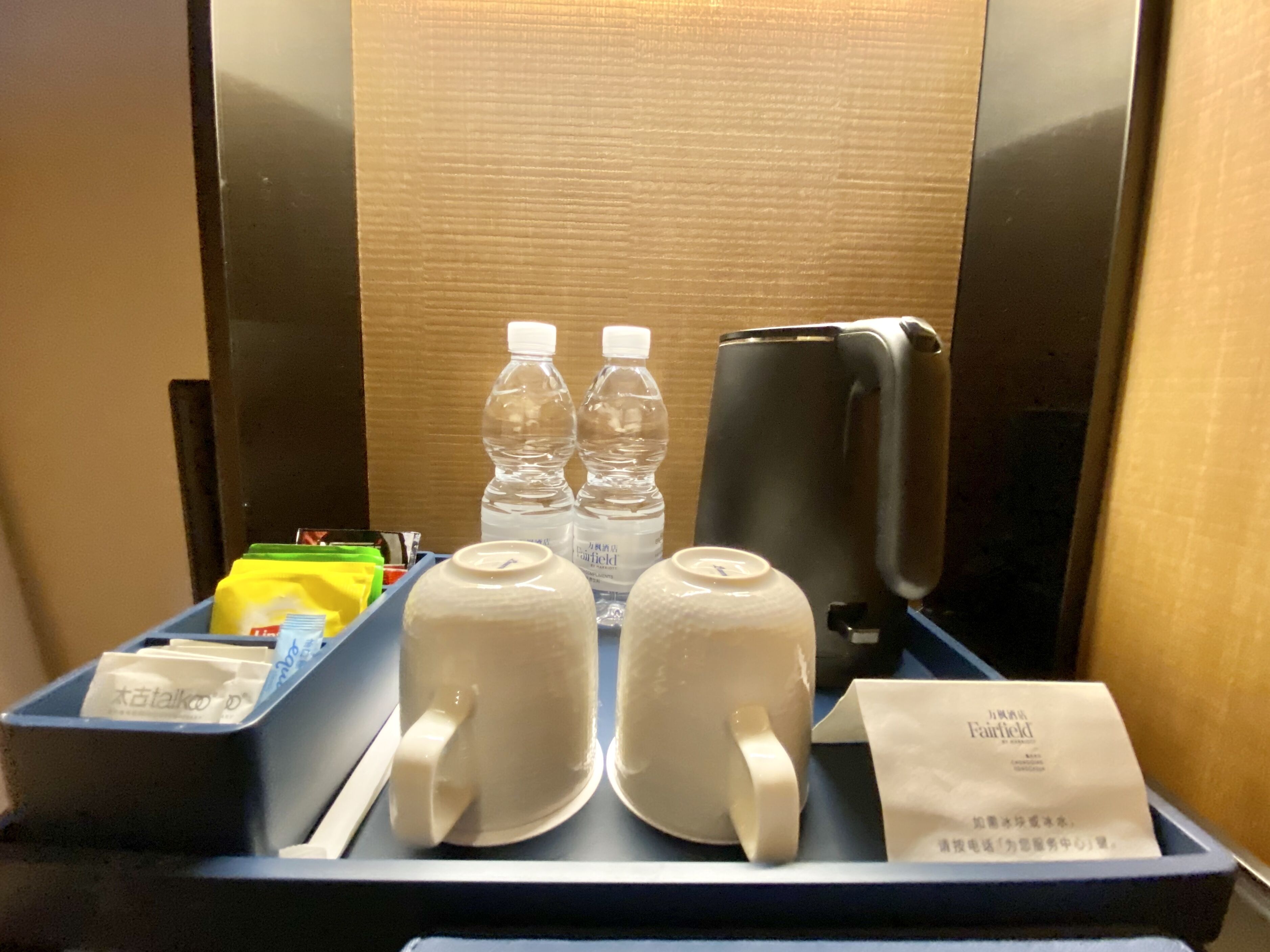 En minibar på hotellet med två flaskor vatten, en kaffebryggare och ett bricka med en näsduk och en liten påse.