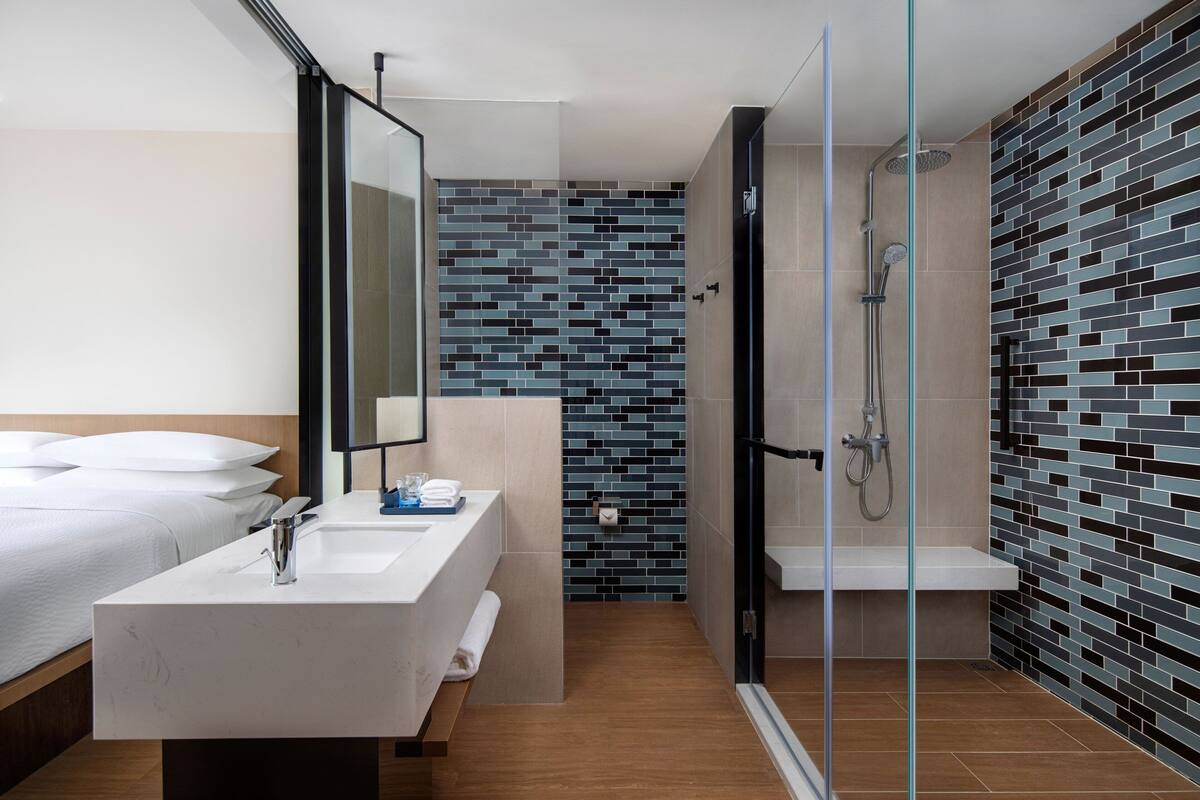 Ein modernes Badezimmer mit Duschkabine aus Glas, einem weißen Waschbecken und einer gefliesten Rückwand.