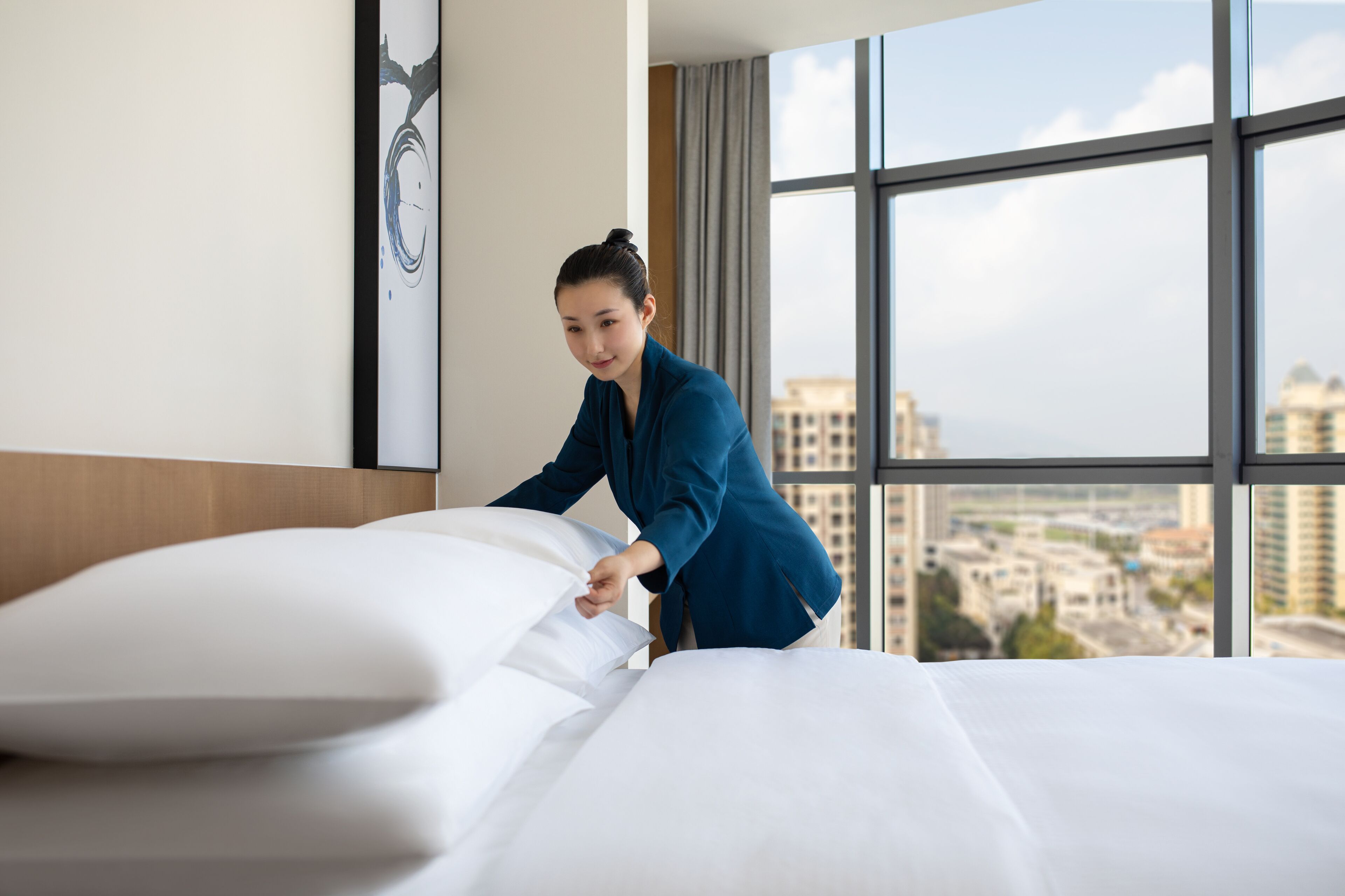 A hotel room with a large window, a neatly made bed, and a city view.