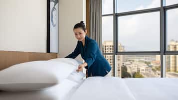 A hotel room with a large window, a neatly made bed, and a city view.