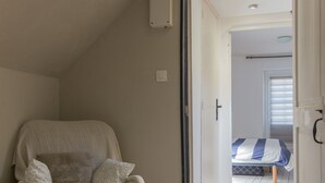 Una stanza con soffitto alto, pavimento in legno, una sedia con cuscini decorati e un letto con copriletto a righe.