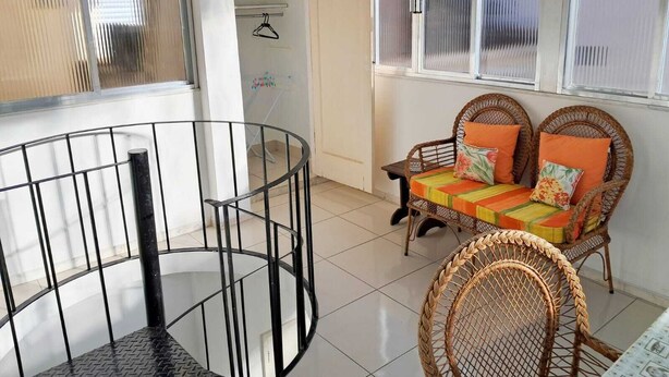 A room with a spiral staircase, wicker furniture, and a view through a window with blinds. - Airy studio apartment in Copacabana, 4 blocks from the beach. (Rio de Janeiro)