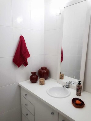 Ein Badezimmer mit weißen Fliesen, einem weißen Waschbecken, einem Spiegel, einem roten Handtuch und einigen Dekorationen auf der Ablagefläche.