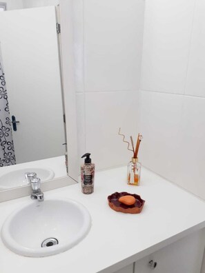 Ein helles Badezimmer mit Waschbecken, Spiegel, Handseife und einer dekorativen Vase mit Kerze.