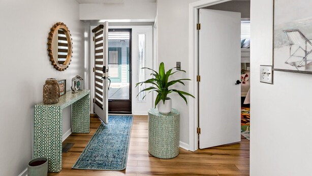 A hallway with a patterned rug, a potted plant, and a mirror on the wall. - Compass Pointe Condominium - Steps to downtown, close to Lake Michigan (Grand Haven)