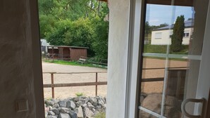 A door leading to an outdoor area with a sandy ground, a wooden fence, and a building in the background. - Dream vacation apartment on an idyllic farm near Eltz Castle (Münstermaifeld)