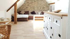 A cozy loft bedroom with a stone wall, wooden beams, a sofa, a dresser, and a wicker chair. - Dream vacation apartment on an idyllic farm near Eltz Castle (Münstermaifeld)
