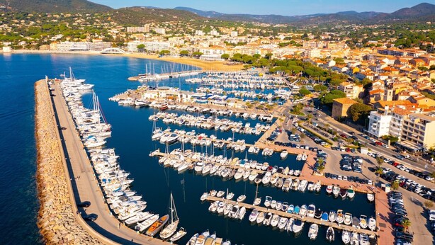 An aerial view of a marina with numerous boats docked, surrounded by residential buildings and hills in the background. - 🏖️ Villa - Swimming pool - 6 people - Near beaches & golf - Wifi (Sainte-Maxime)