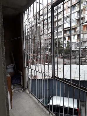 A balcony with metal railings, a view of a multi-story building, and a parked car in the background.