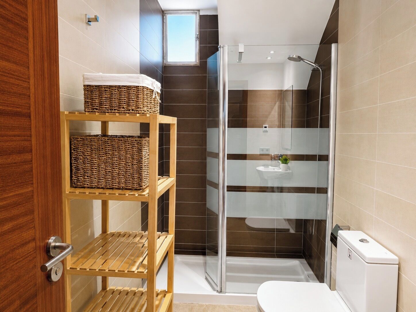 A modern bathroom with a glass shower enclosure, a toilet, and a wooden shelf with baskets.