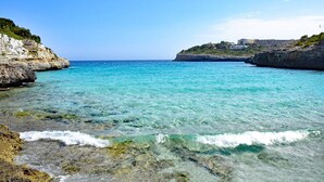 A coastal scene with clear turquoise water, rocky shores, and buildings on a hill in the background. - Casa Descansa - vacation to feel good, enjoy and relax! (Cala Mendia)