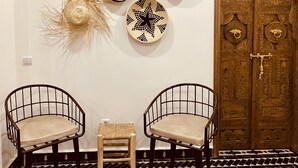 A room with a wooden door, two wire chairs, a small stool, and decorative wall art. - Manzilisurfhouse (Tamraght)