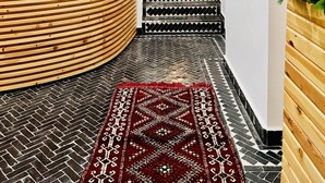 A reception area with a wooden reception desk, a laptop, a hanging light fixture, a staircase with patterned steps, and a red wall-mounted cabinet. - Manzilisurfhouse (Tamraght)