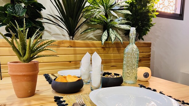 A wooden table with a white plate, bowls, cutlery, and a potted plant. - Manzilisurfhouse (Tamraght)