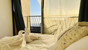 A hotel room with a bed, a window with a view of the city, and a balcony with a railing. - Manzilisurfhouse (Tamraght)