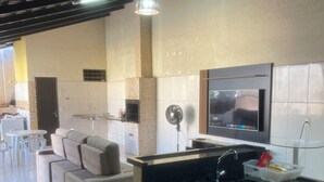 A modern kitchen with a built-in island, a dining area with a sofa, and a TV mounted on the wall. - House in gated community with privileged location (Aparecida de Goiânia)