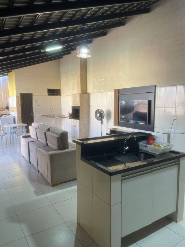 A modern kitchen with a built-in island, a dining area with a sofa, and a TV mounted on the wall.