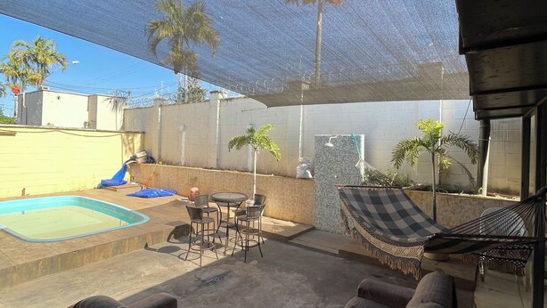A covered outdoor area with a pool, lounge chairs, and a hammock. - House in gated community with privileged location (Aparecida de Goiânia)
