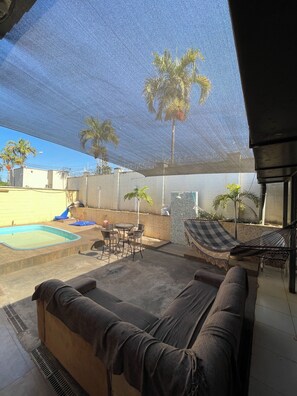 A covered outdoor area with a pool, lounge chairs, and a hammock.