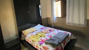 A bedroom with a bed, a window with curtains, an air conditioning unit, and a small window with blinds. - House in gated community with privileged location (Aparecida de Goiânia)