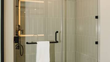 Une douche fermée par des parois en verre, dotée d’un pommeau de douche à main, d’un porte-serviettes et de toilettes.