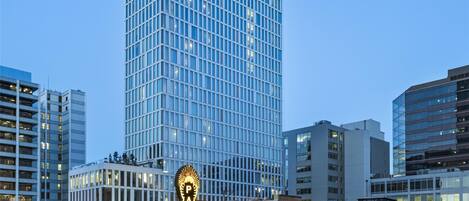 A modern high-rise building with a glass facade, surrounded by other buildings and a historic theater with a marquee.