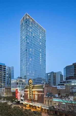 A modern high-rise building with a glass facade, surrounded by other buildings and a historic theater with a marquee. - Hyatt Centric Congress Ave Austin (Austin)